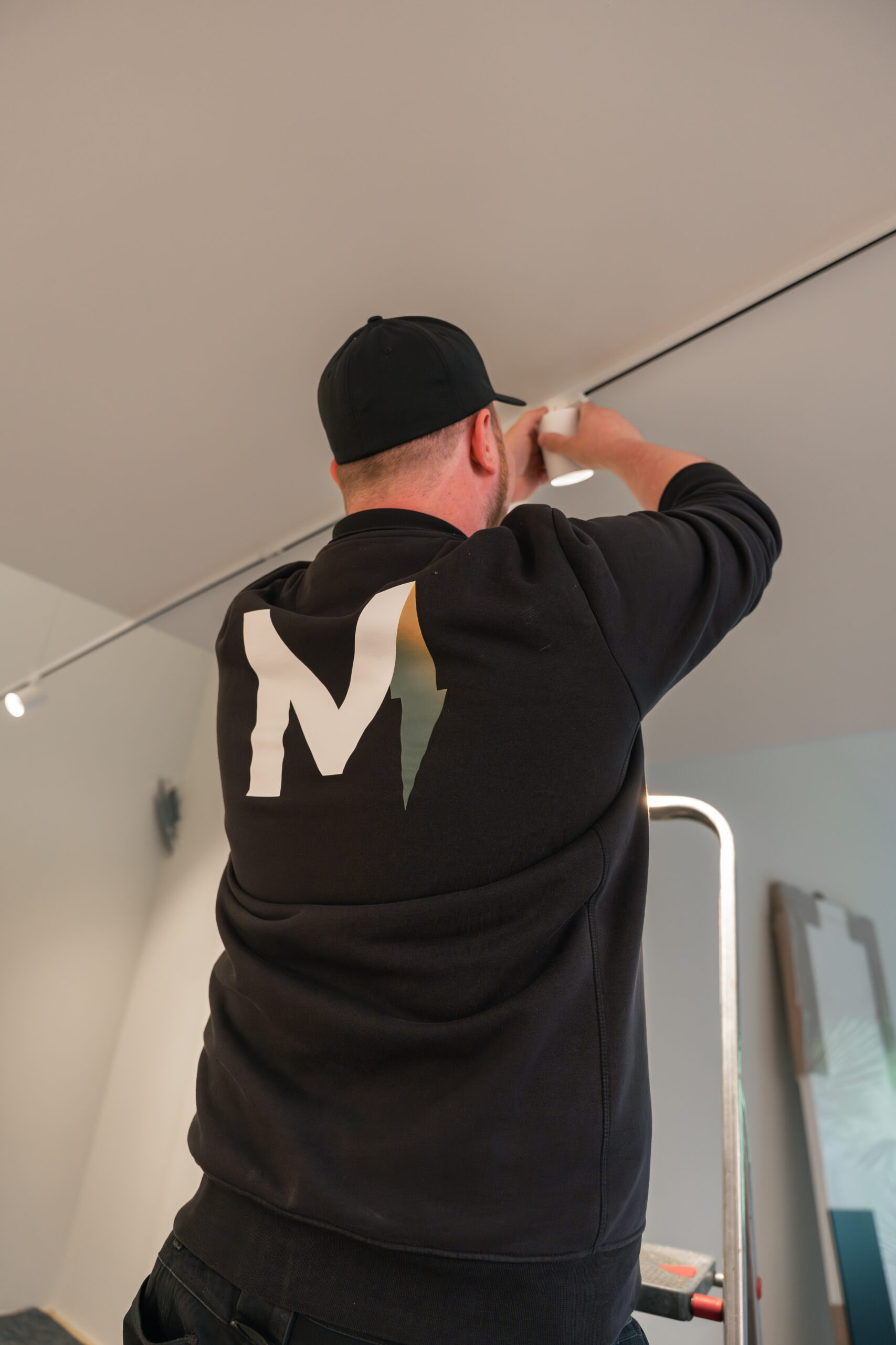 Elektriker von Elektro Mersmann montiert Deckenspot am Schienensystem auf der Leiter – Beleuchtungsinstallation in Harsewinkel